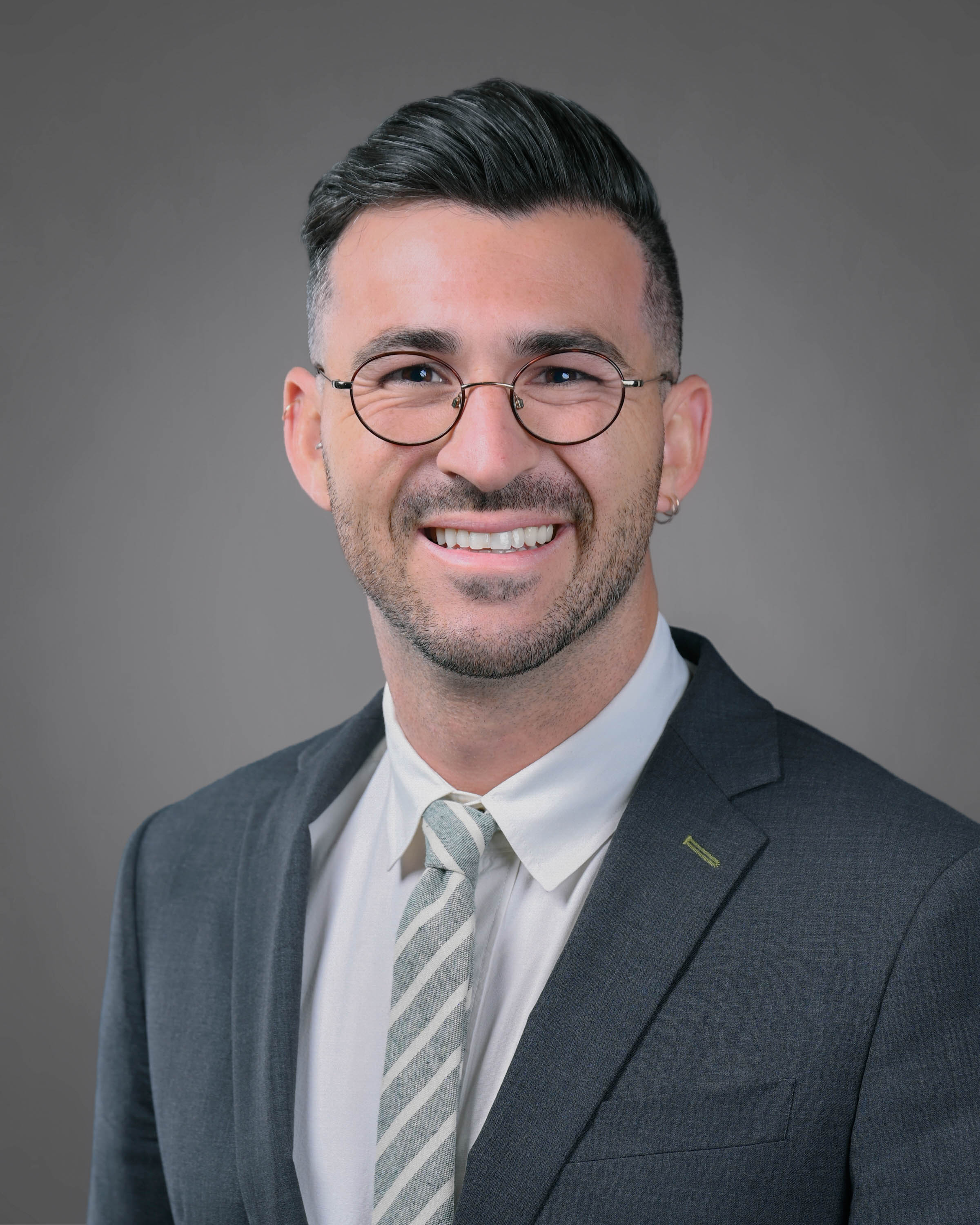 Smiling man with eye glasses and a short beard in a grey suit jacket with light er gray tie